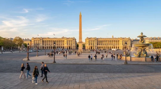 Vue grand angle de la Place de la Concorde au coucher du soleil avec l'Obélisque au centre et des touristes marchant en arrière-plan